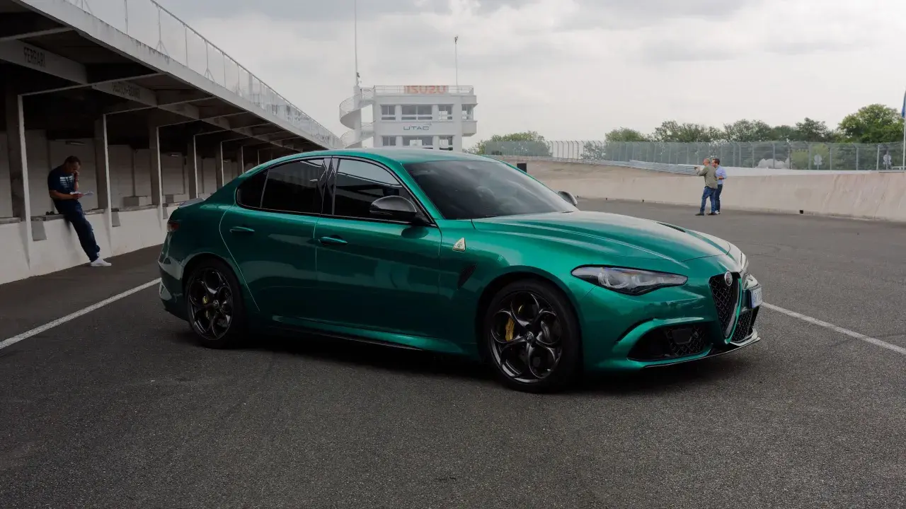 Zielona Alfa Romeo Giulia Quadrifoglio na torze wyścigowym, z wieżą kontrolną w tle.