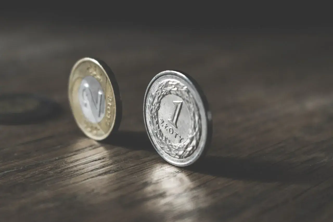 Dwie polskie monety, 1 złoty i 2 złote, na drewnianym blacie. Marzenie o pensji 6500 brutto.