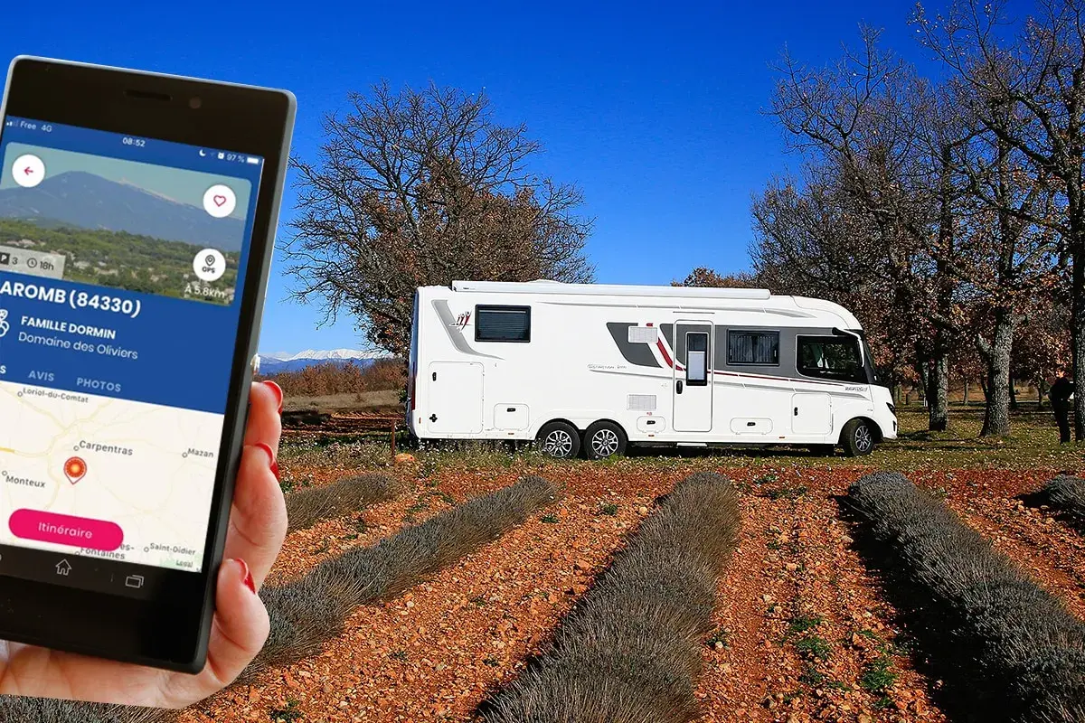 Une application camping-car à la ferme guide vers le Domaine des Oliviers. Un camping-car blanc est garé dans un champ de lavande séchée.