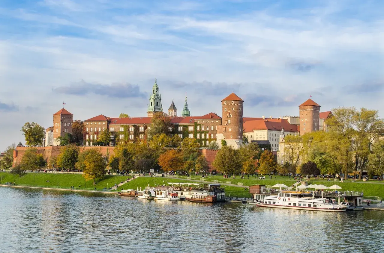 Zabytkowe miasto nad Wisłą, Wawel w jesiennej odsłonie, z łodziami cumującymi przy brzegu.