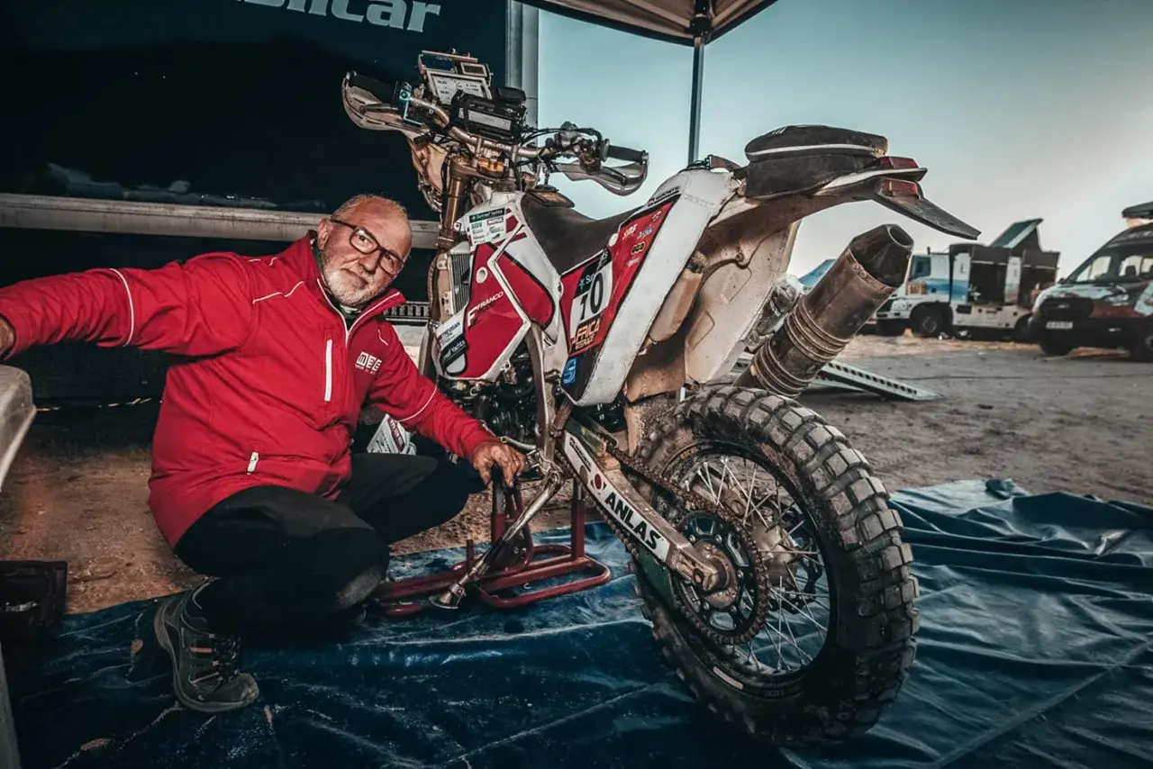 Uomo in giacca rossa vicino a moto da cross sporca, pronto a capire come pulire il motore dopo una gara.