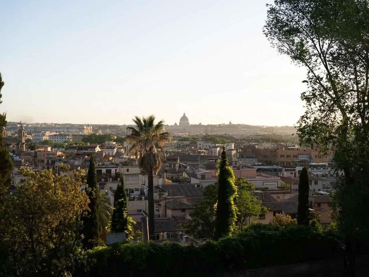Panoramic view of Rome with St. Peter's Basilica dome in the distance, framed by trees and greenery.