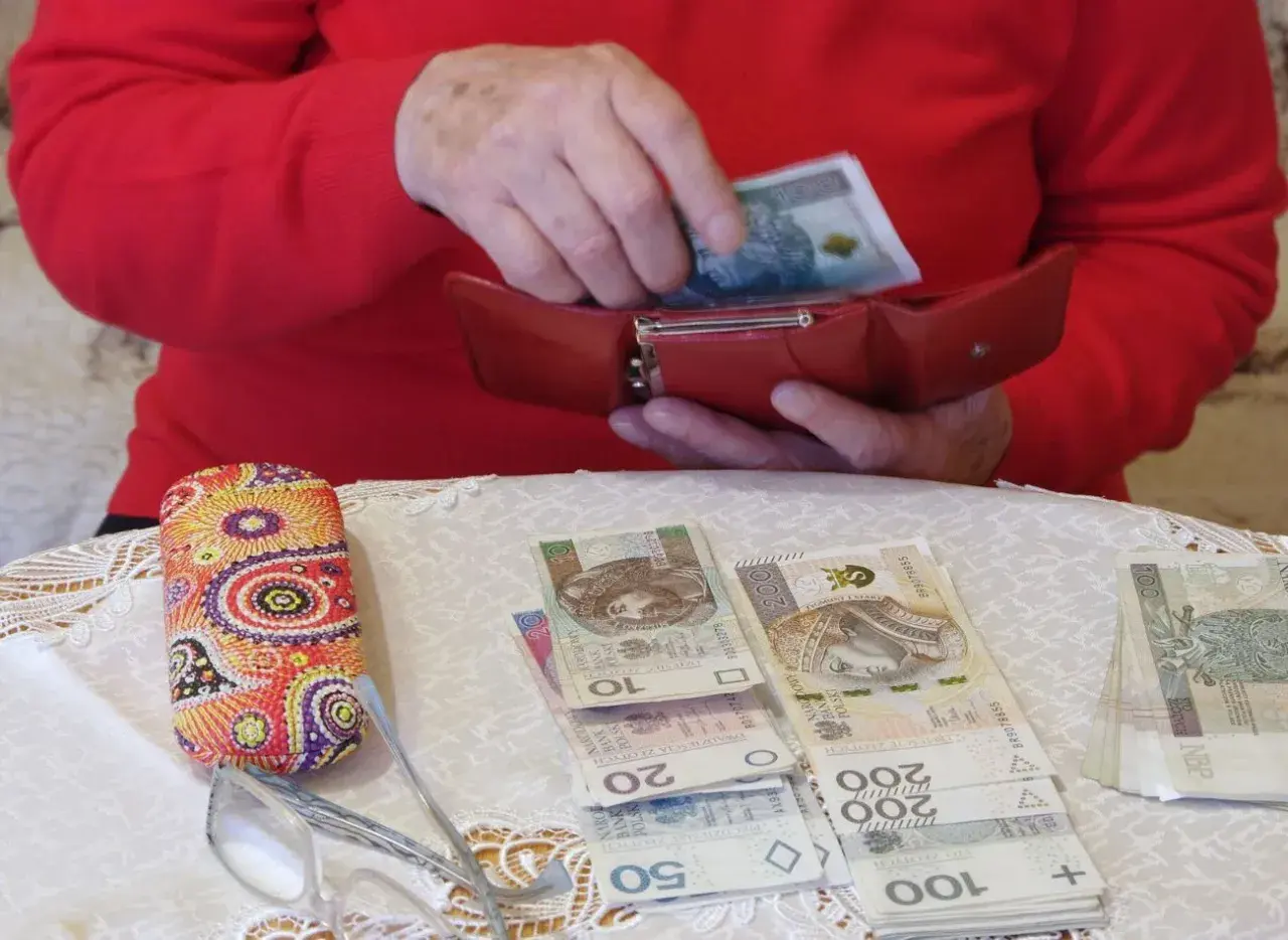 Dłonie chowają banknot 100 zł do czerwonego portfela. Obok leżą pieniądze, okulary i etui. To pokazuje, gdzie trzymać pieniądze.