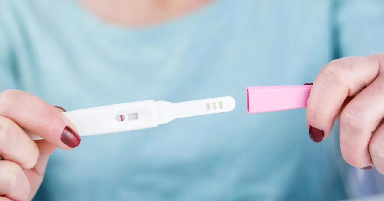 Dłoń trzyma test ciążowy z widocznym jednym paskiem. Rozważana jest opcja przerwania ciąży, być może z użyciem mizoprostolu.