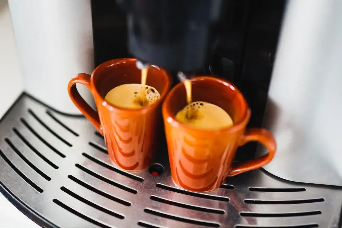 Dwa pomarańczowe kubeczki wypełniają się aromatycznym espresso. Idealny poranek z kawą.