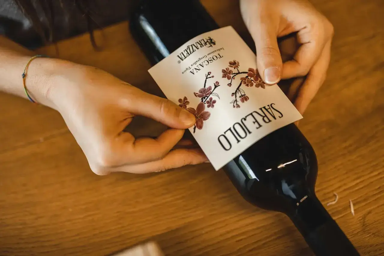 Mani che applicano l'etichetta a una bottiglia di vino rosso, forse il best wine in Tuscany.