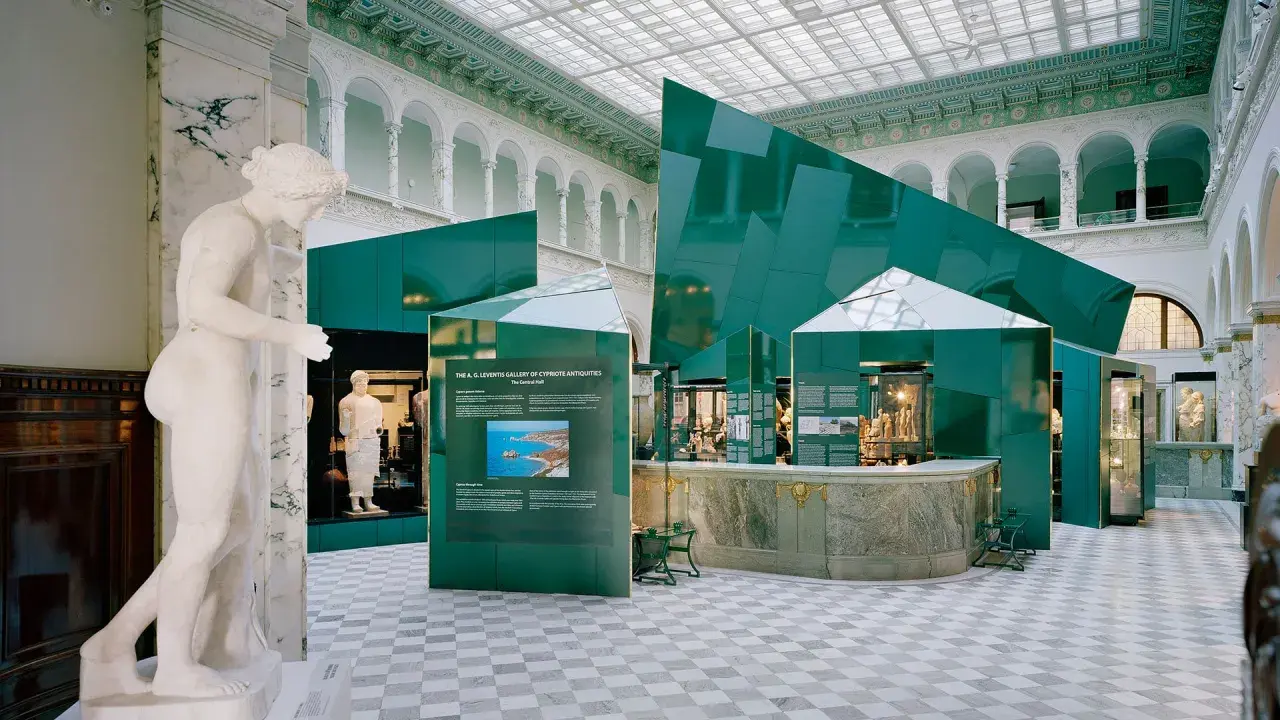 En marmorstaty i förgrunden på Medelhavsmuseet Stockholm. Gröna, geometriska installationer och antika föremål visas i den ljusa hallen.