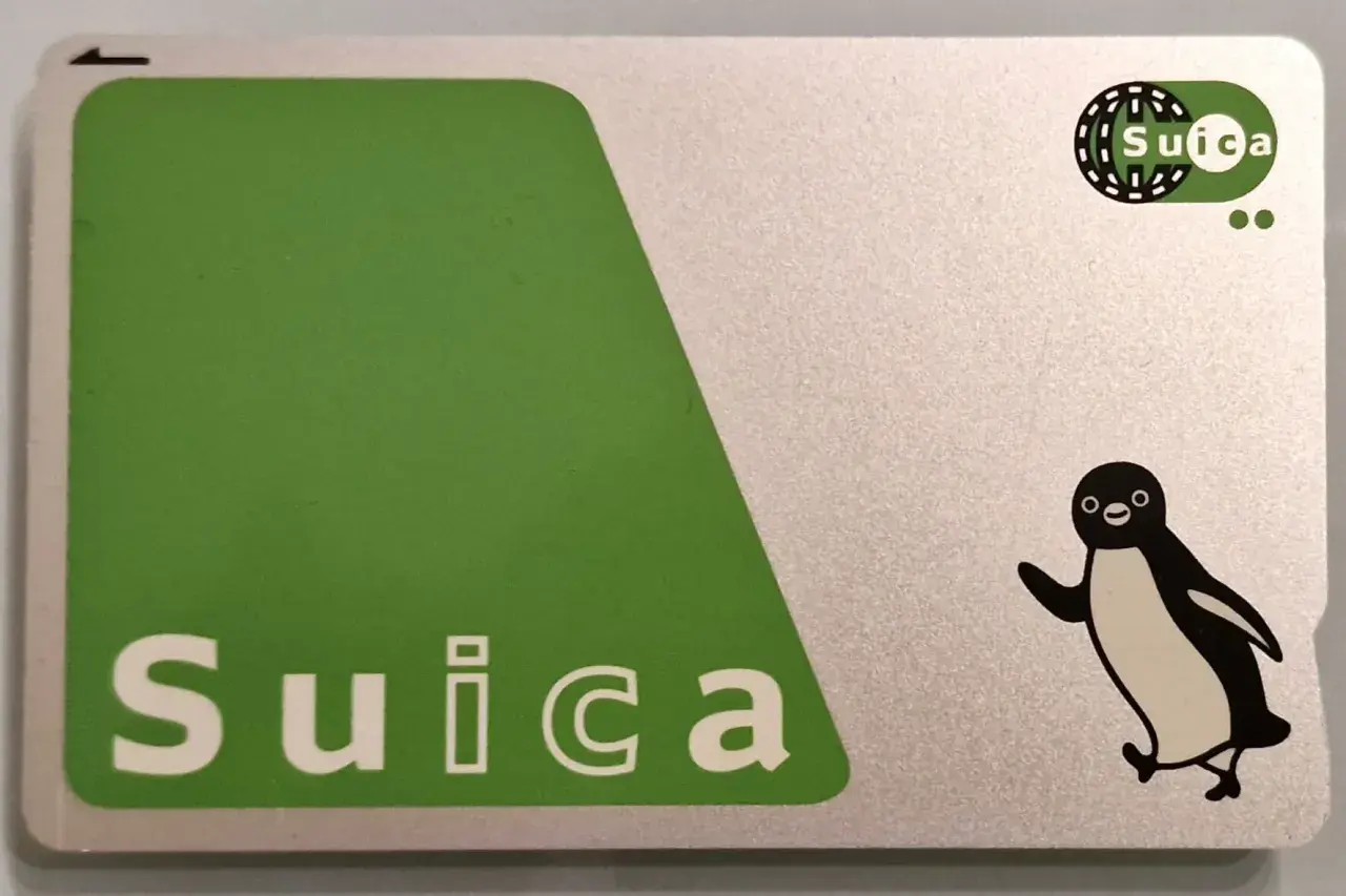 Eine Suica-Karte mit einem fröhlichen Pinguin-Motiv. Die Karte ist silberfarben mit einem großen grünen Feld und dem Schriftzug "Suica".