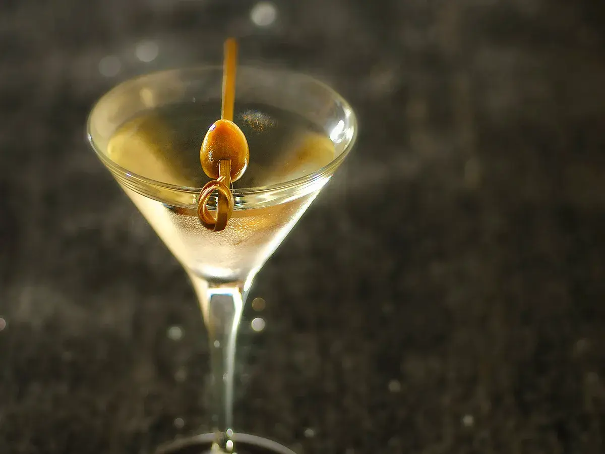 Un verre à martini rempli d'un cocktail clair, garni d'une olive sur un cure-dent. Une image parfaite pour une vodka martini recette.