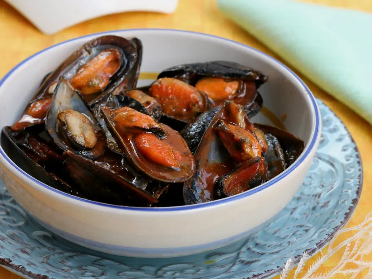 Un invitante sautè di cozze, succulente e profumate, servite in una ciotola bianca con bordo blu.