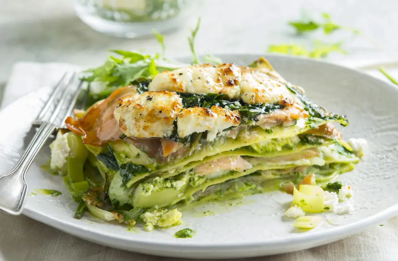 Une part de lasagne saumon épinard, gratinée au fromage, servie avec une salade verte.