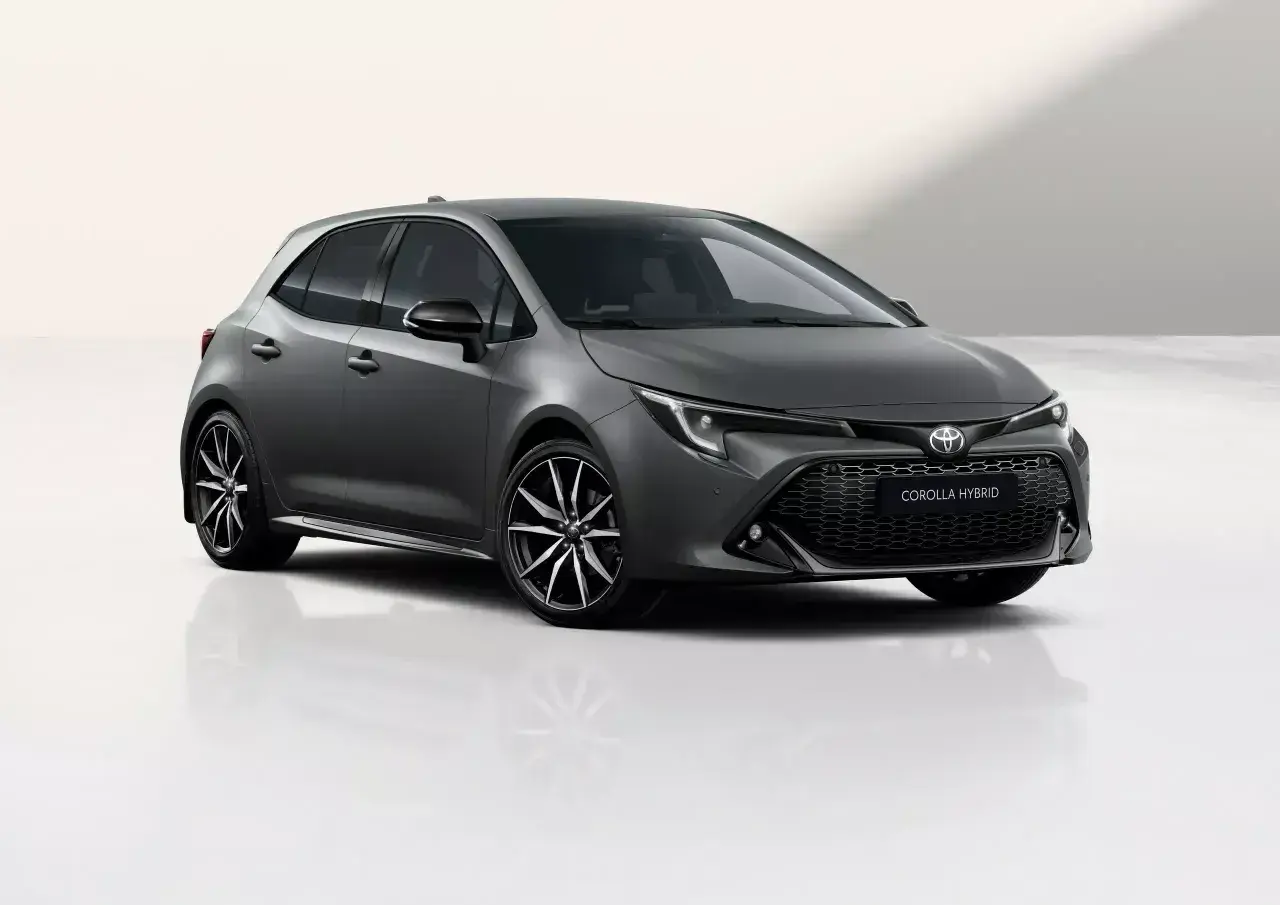 Szary hatchback Toyota Corolla 1.8 Hybrid z czarnymi felgami stoi na białym tle.