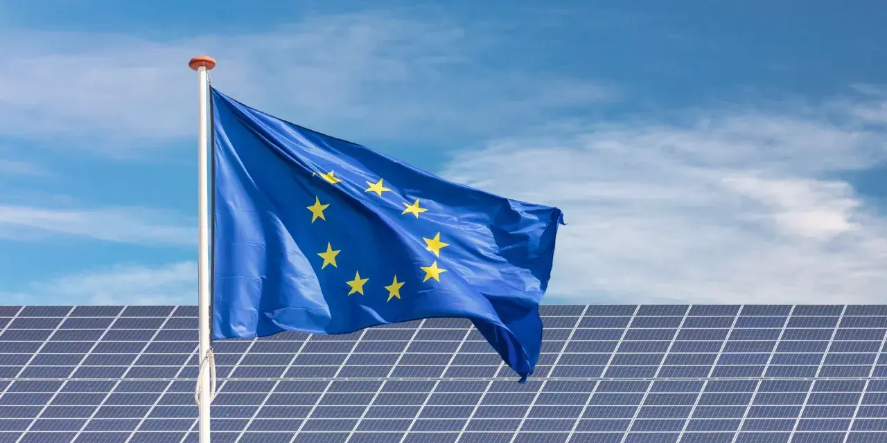 Bandera de la UE ondeando sobre placas solares en Extremadura, símbolo de ayudas para la energía limpia.