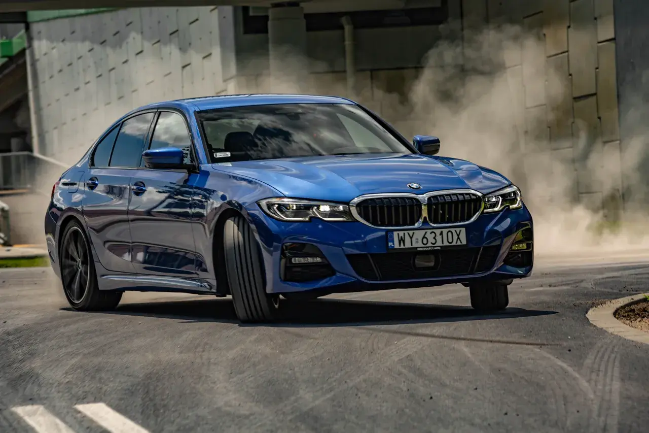 Niebieskie BMW 330i G20 w zakręcie, unosząc tumany kurzu.