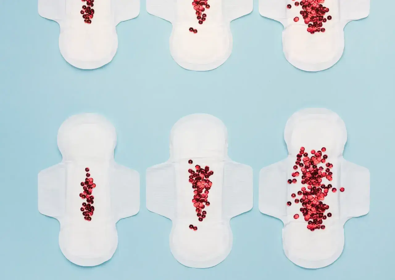 Toallas sanitarias con lentejuelas rojas que simulan el flujo menstrual, representando la dismenorrea que es.