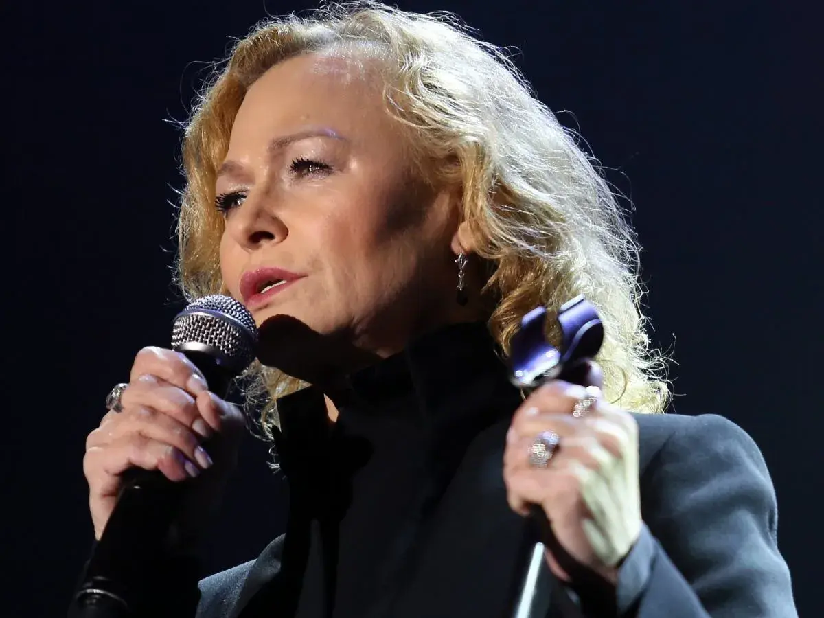 Kobieta z blond włosami śpiewa do mikrofonu. Czy to piotr loretz pierwszą żoną?
