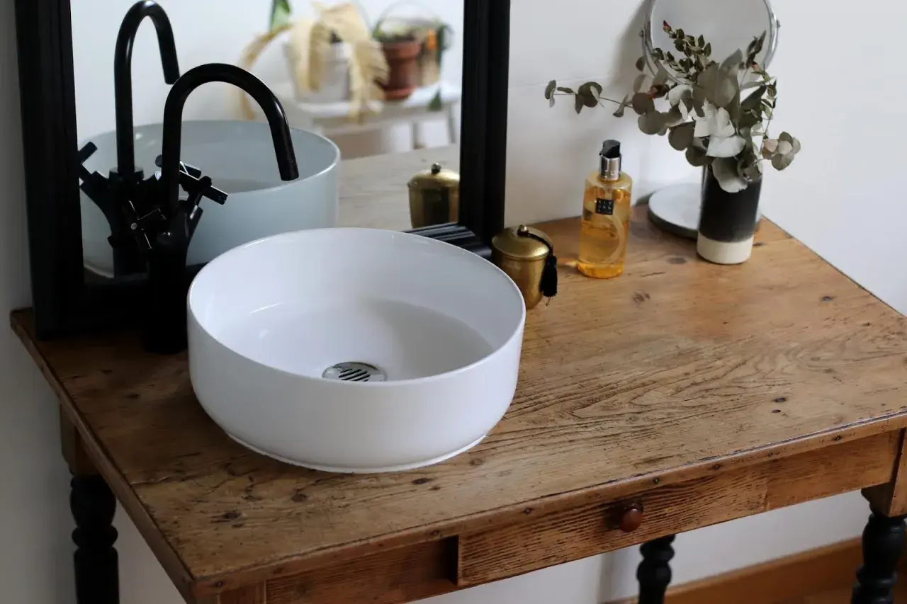 Un plan pour créer son meuble de salle de bain : vasque blanche, robinetterie noire, miroir et accessoires déco sur un meuble ancien.