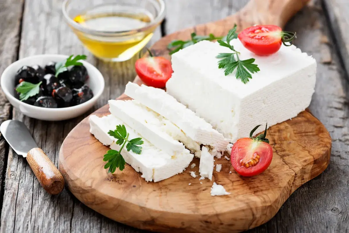 Una porzione feta fresca, tagliata a fette, con pomodorini e olive nere su un tagliere di legno.
