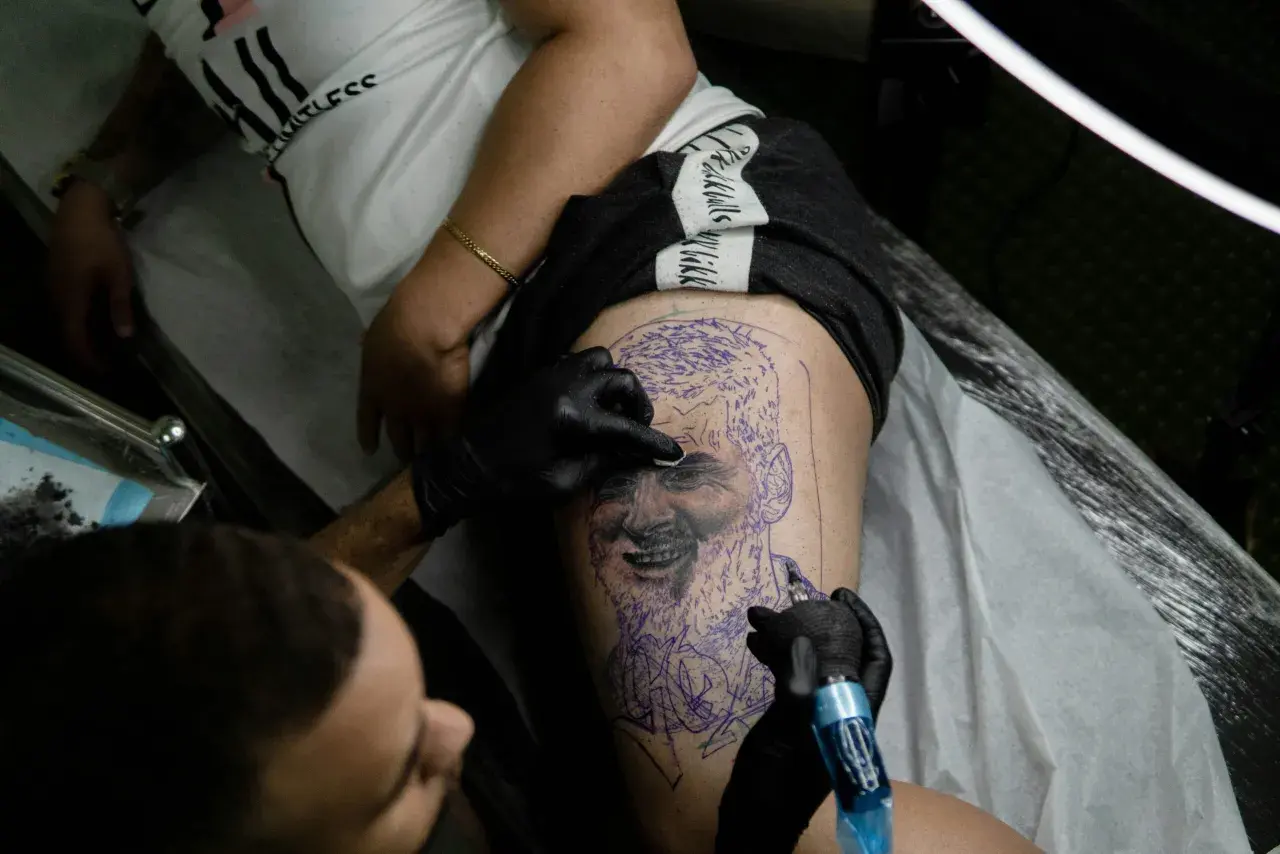 Un tatuador trabaja en un retrato en la pierna de un cliente, demostrando la habilidad de los mejores tatuadores de España.