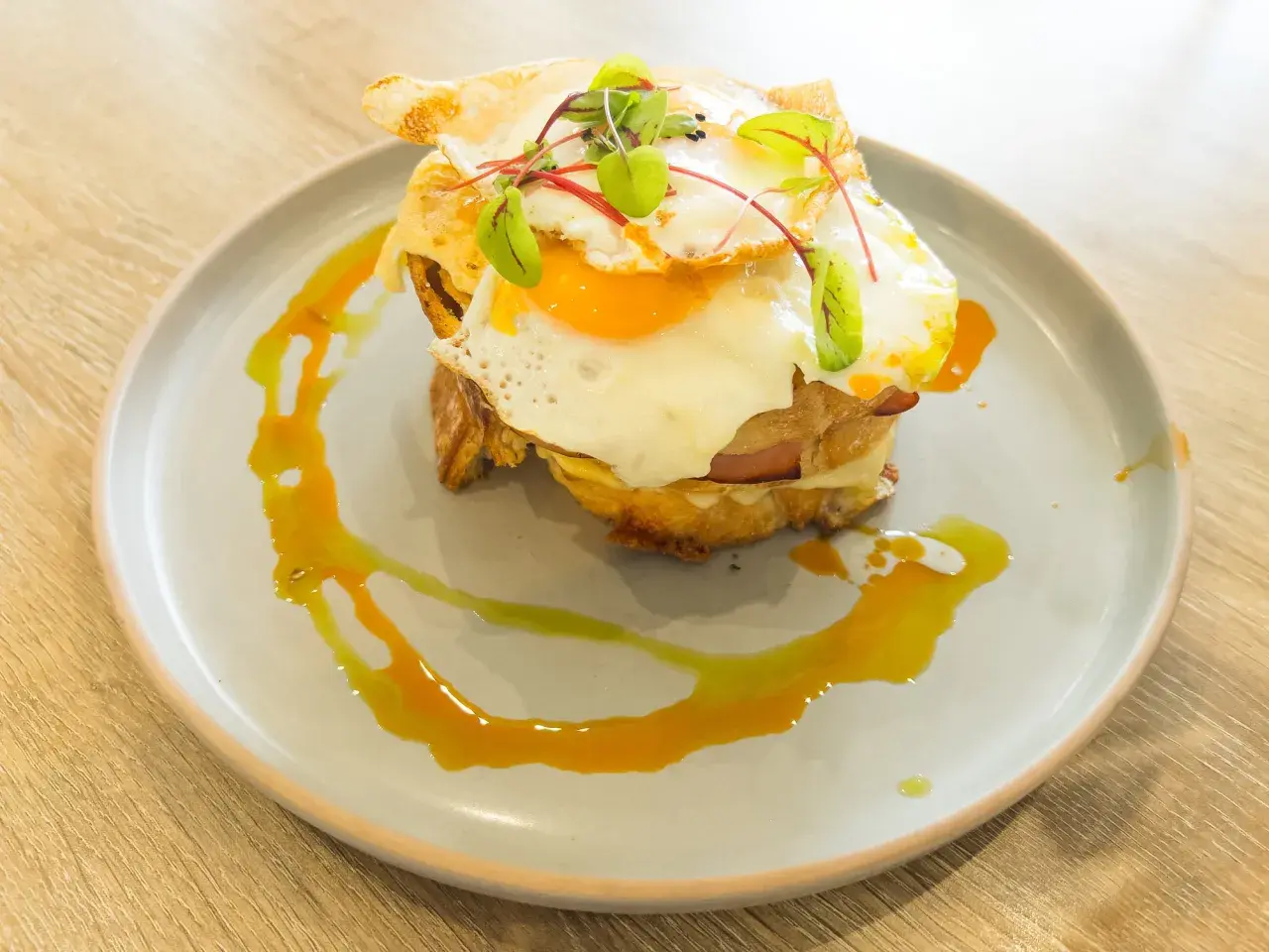 Un délicieux croque madame avec un œuf au plat coulant, du jambon et du fromage fondu, garni de jeunes pousses et servi sur une assiette avec un filet de sauce.