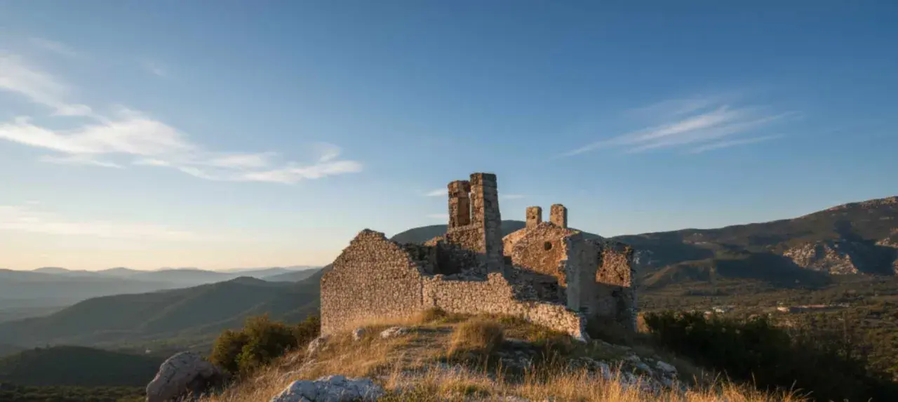 Ruines d'un château médiéval à Châteauneuf-les-Moustiers, baignées par la lumière dorée du soleil couchant, dominant un paysage de collines verdoyantes.