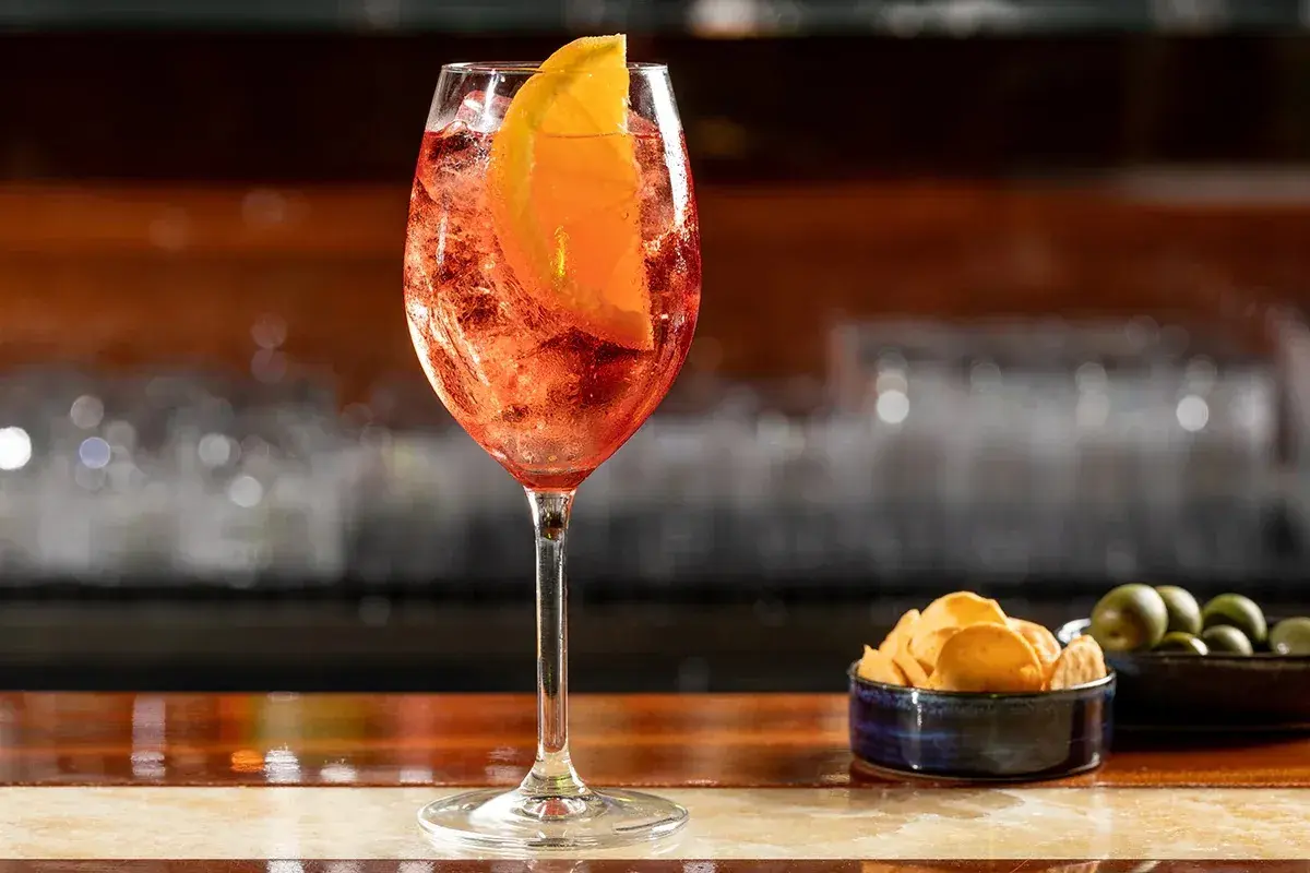 Un bicchiere di Aperol Spritz, rinfrescante e colorato, pronto per un aperitivo con patatine e olive.