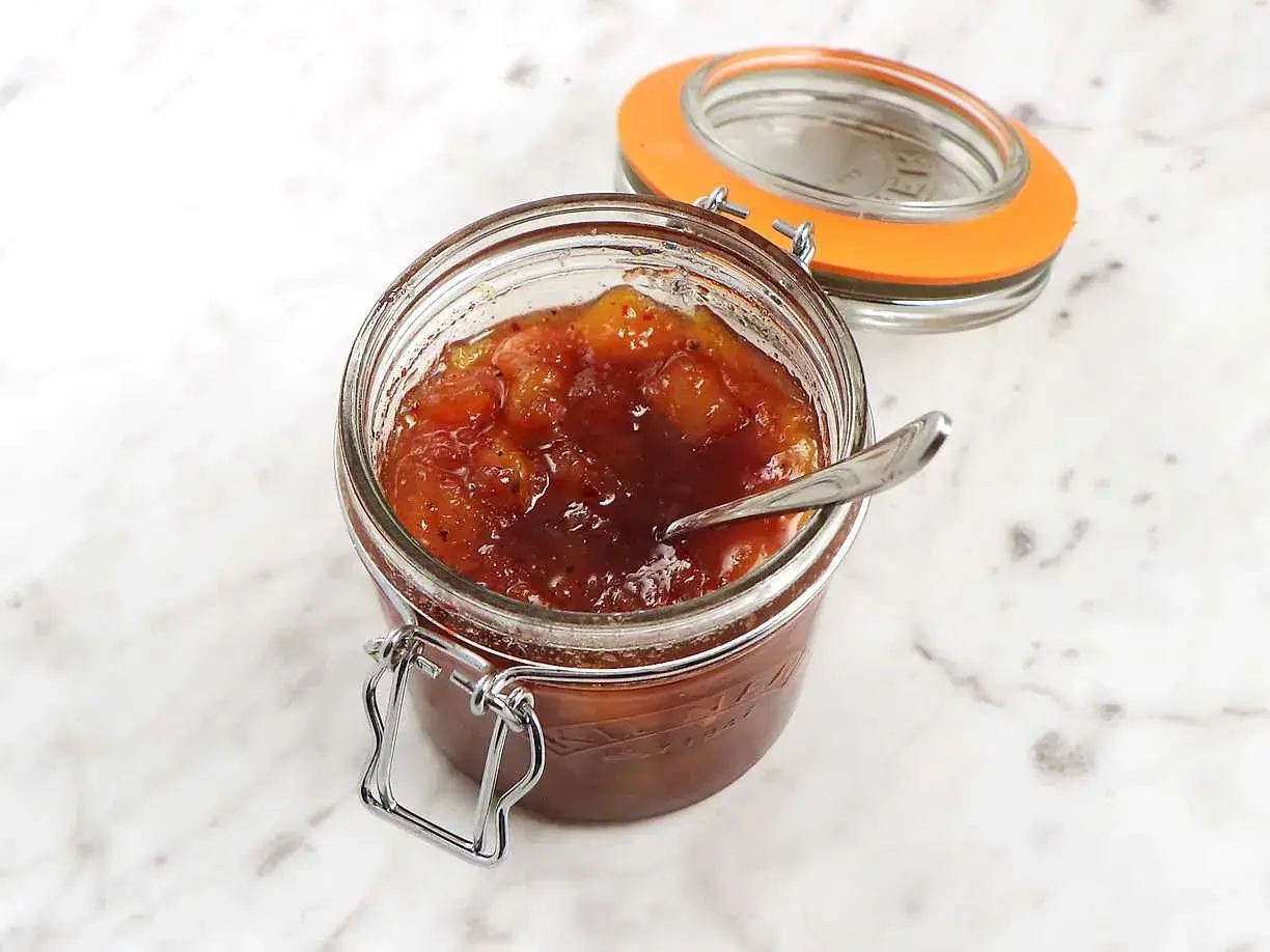 En burk med hemlagad mango chutney, perfekt för ditt nästa mango chutney recept. En sked vilar i den söta, kryddiga blandningen.