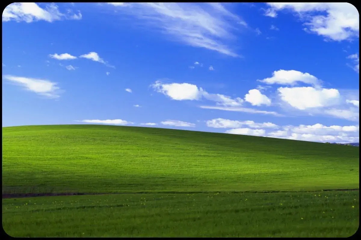 Zielone wzgórze pod błękitnym niebem z chmurami, ikoniczny widok z **win xp virtual machine**.