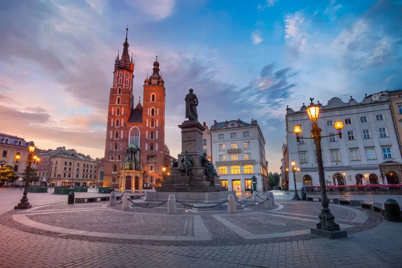 Krakowski rynek główny o zachodzie słońca. Monumentalna Bazylika Mariacka i pomnik Adama Mickiewicza w blasku latarni.