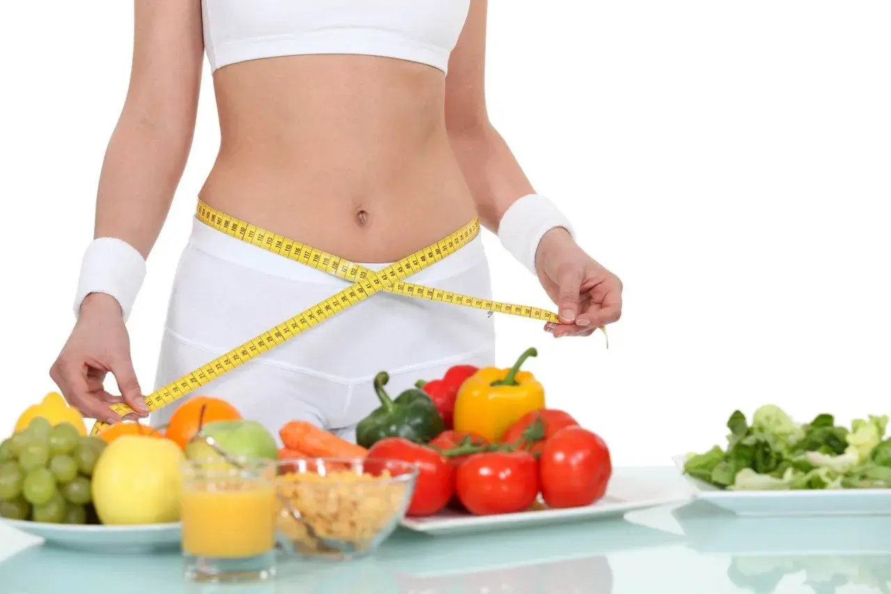 Kobieta mierzy talię centymetrem. Obok zdrowe jedzenie: owoce, warzywa, płatki. Dieta 1500 kcal efekty w zasięgu ręki!