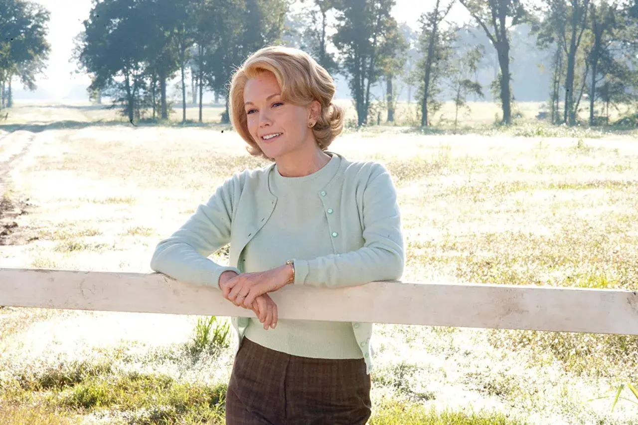 Diane Lane w pastelowym sweterku opiera się o płotek, przypominając scenę z jednego z jej filmów.