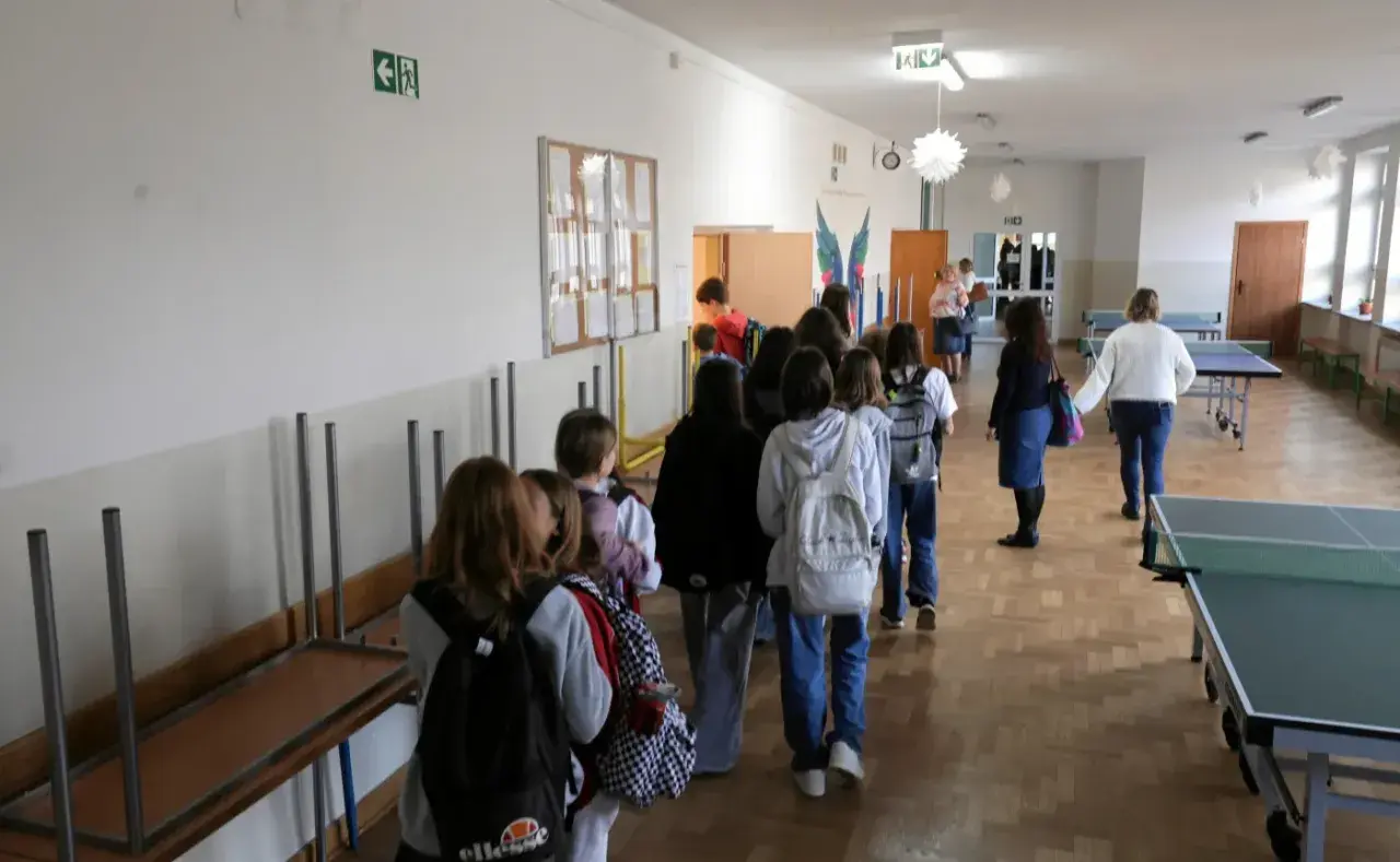 Uczniowie w kolejce na szkolnym korytarzu, w tle stoły do tenisa stołowego.