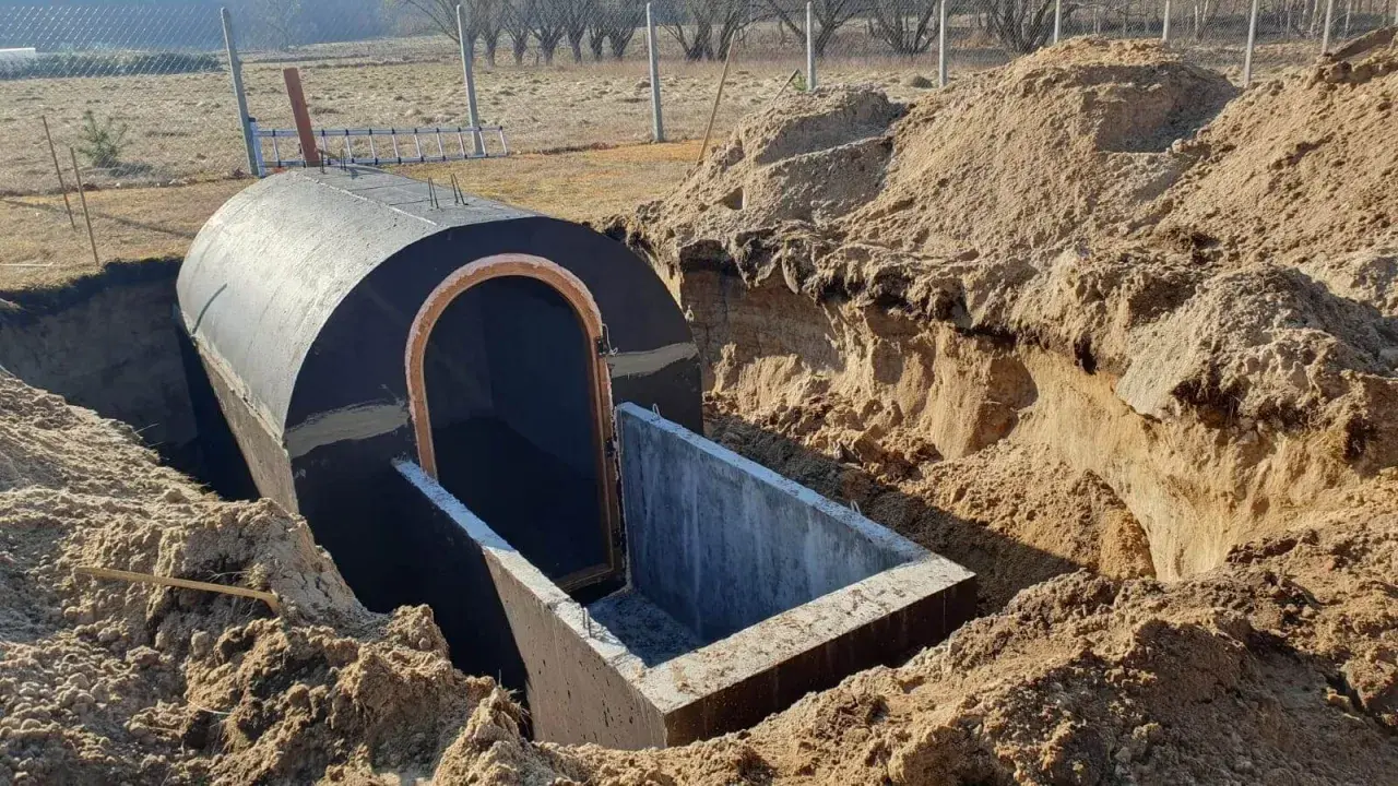 Budowa piwnicy ziemianki w trakcie. Okrągły, betonowy tunel z wejściem wkopany w ziemię, otoczony usypanym piaskiem.
