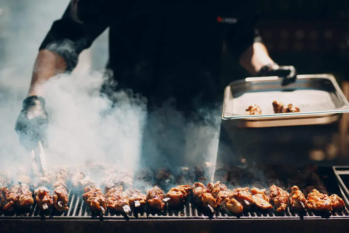 Fleischspieße brutzeln auf dem Grill, Rauch steigt auf. Ein Koch bereitet ein italienisches Grillfest vor.