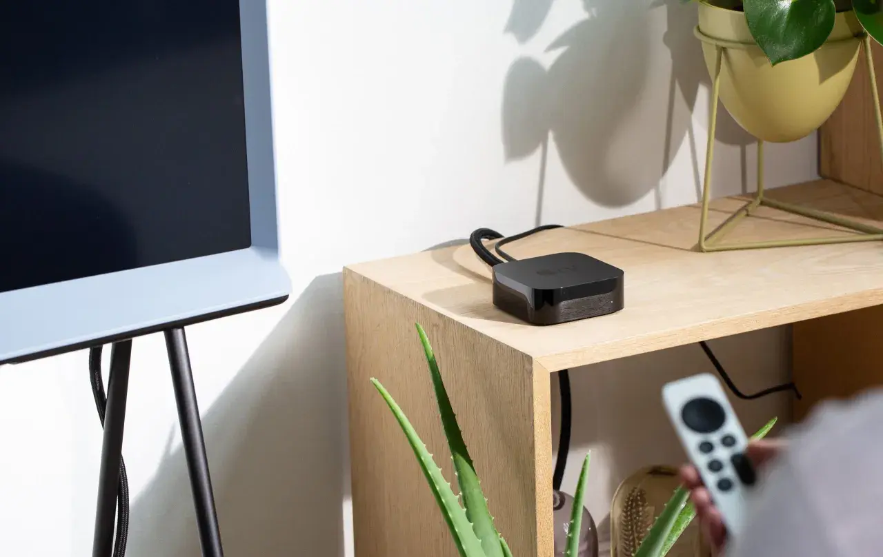 Ein Apple TV-Gerät liegt auf einem Holzregal neben einem alten Fernseher. So verbindest du deinen alten Fernseher mit dem Internet.