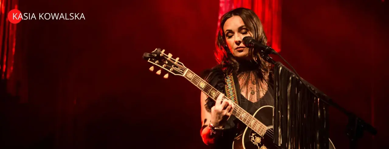 Kasia Kowalska na scenie, grając na gitarze i śpiewając. Jej utwory poruszają serca publiczności.