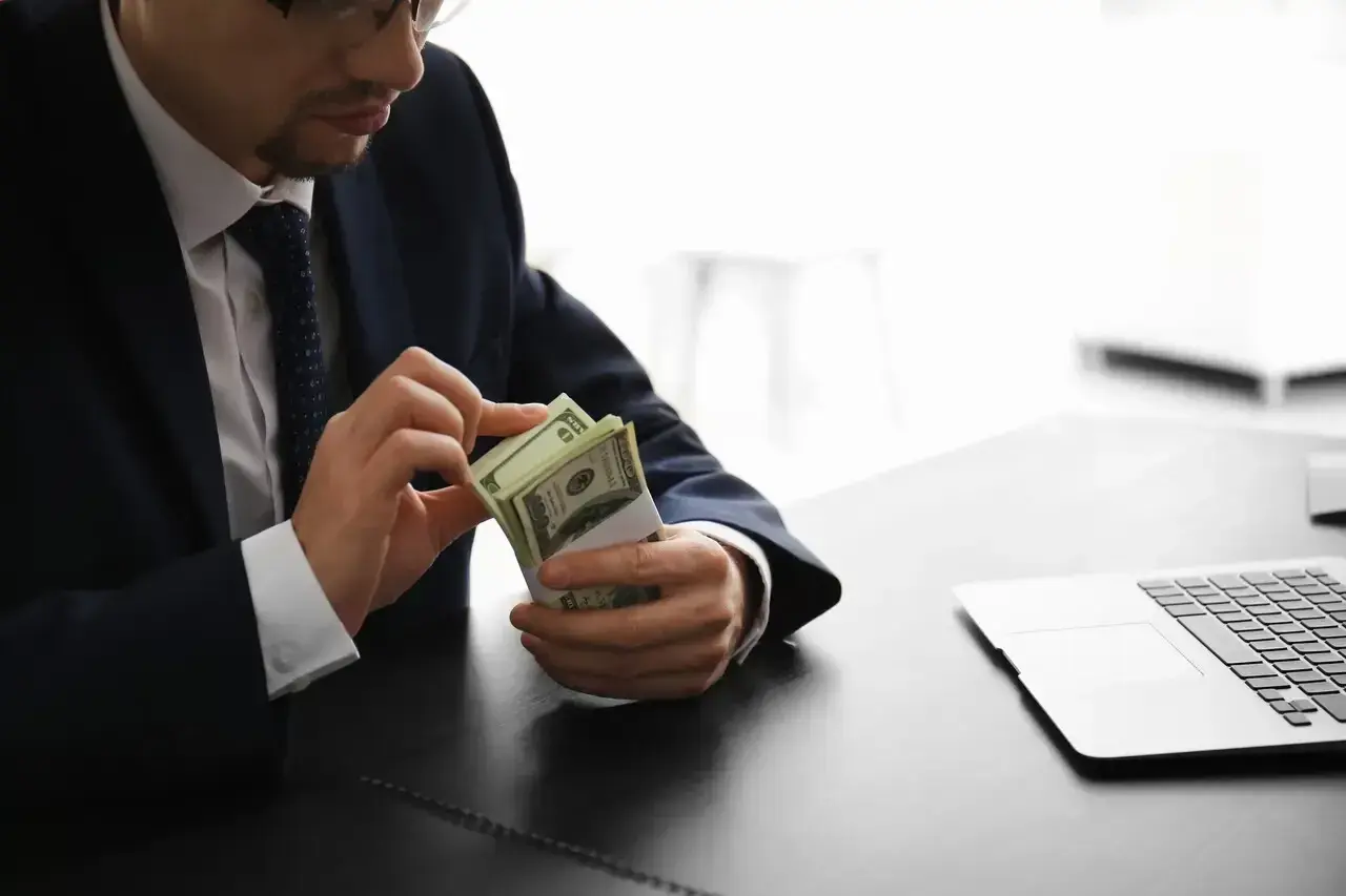 Mężczyzna w garniturze liczy banknoty dolarowe przy biurku. Jego praca w banku wymaga precyzji.