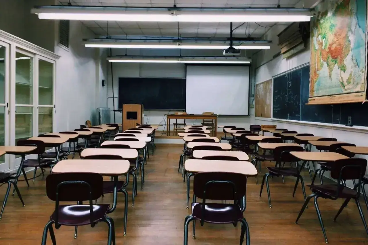 Pusta sala lekcyjna z rzędami ławek i krzeseł, tablicą i mapą świata.