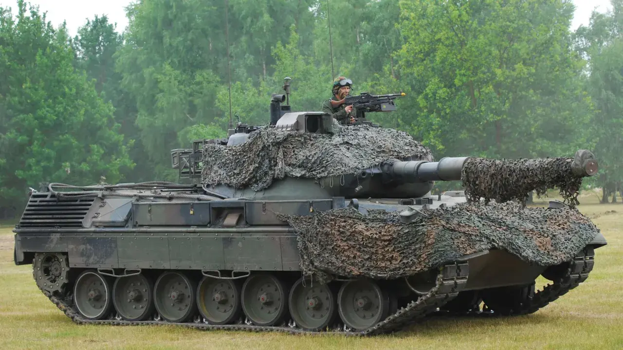Ein Leopard 1 Panzer mit Tarnnetz und einem Soldaten am Maschinengewehr. Sein Gewicht ist beeindruckend.