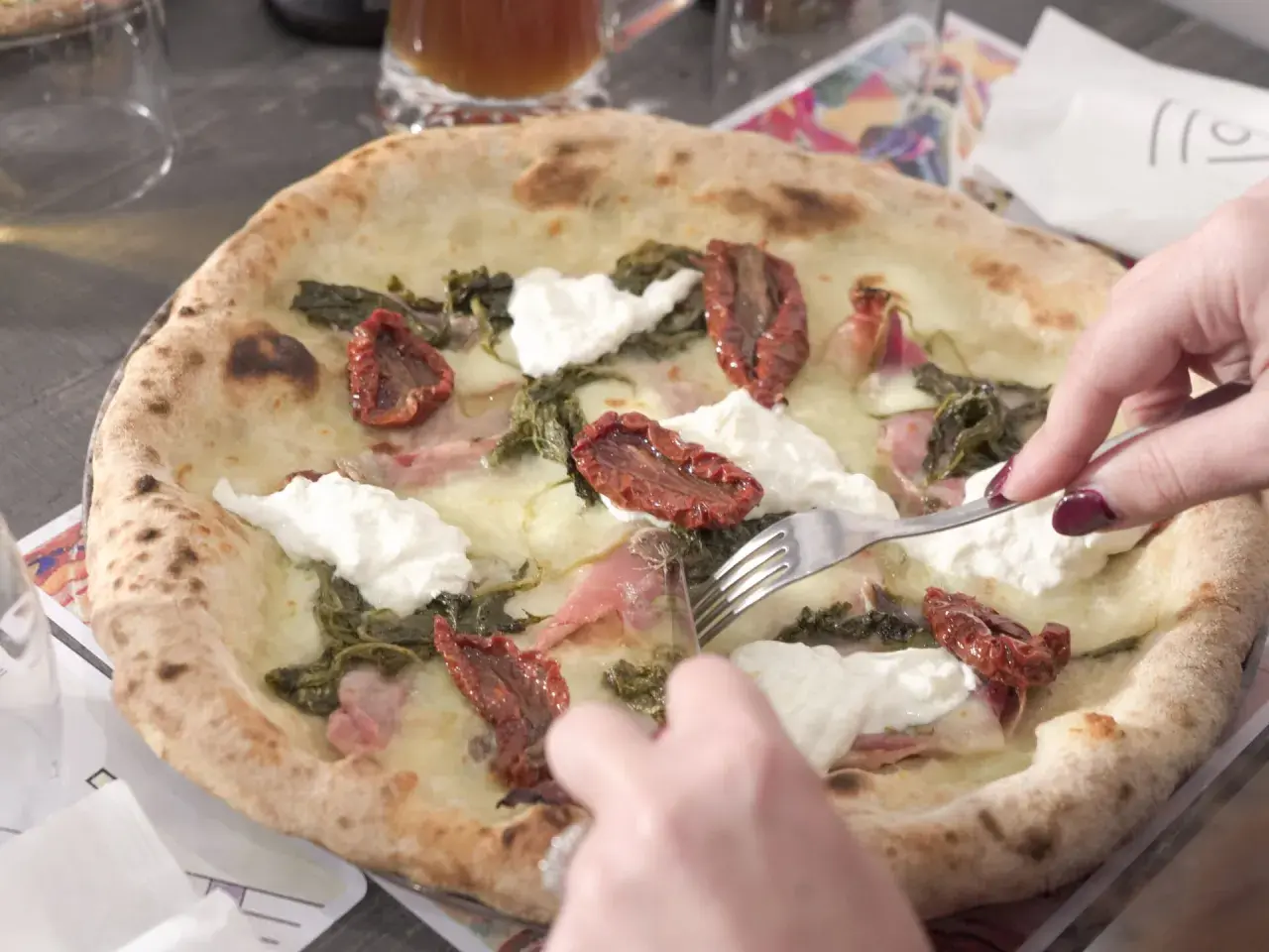 Una puccia Otranto, con pomodori secchi, burrata e verdure, viene tagliata con una forchetta.