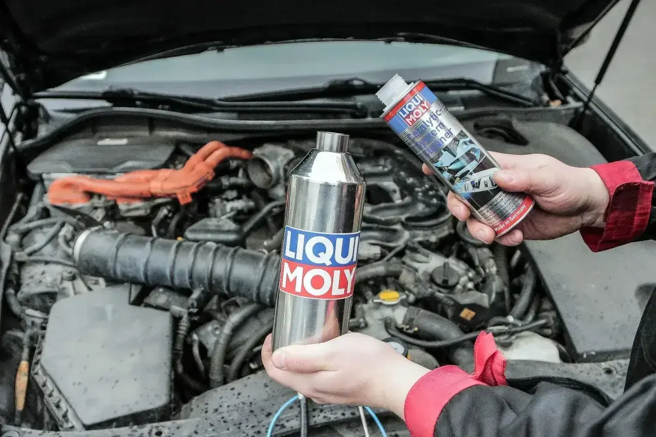 Czyszczenie katalizatora za pomocą preparatu Liqui Moly. Dwie ręce trzymają metalową butelkę i puszkę z płynem.