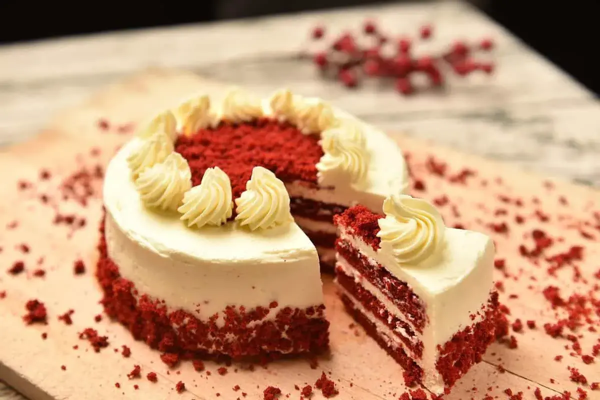 Pastel red velvet con glaseado blanco y decoraciones de crema. Una rebanada muestra las capas rojas y blancas. ¡Perfecto para tu próxima red velvet receta!