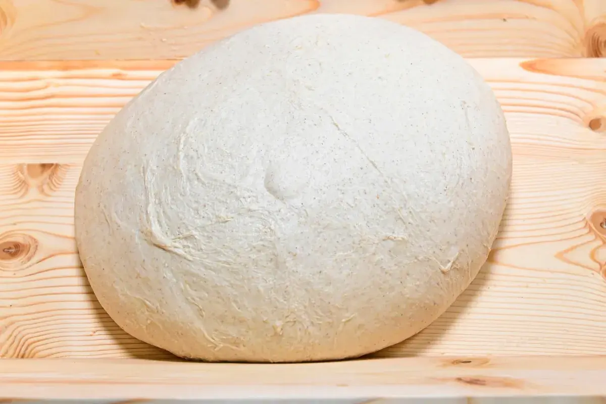 Impasto lievitato per pizza in casa, pronto per essere steso su un tagliere di legno.