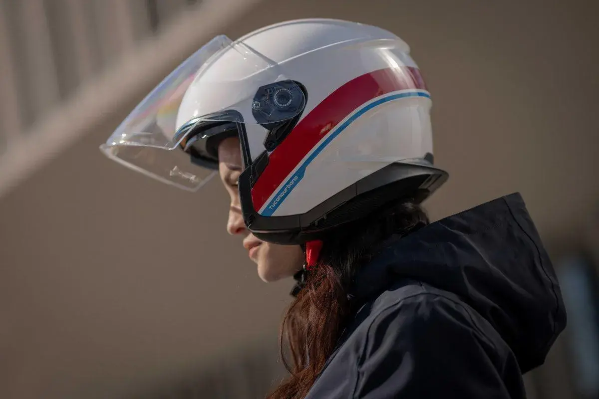 Donna con casco bianco e strisce rosse e blu, un esempio di diversi tipi di casco per la sicurezza in moto.