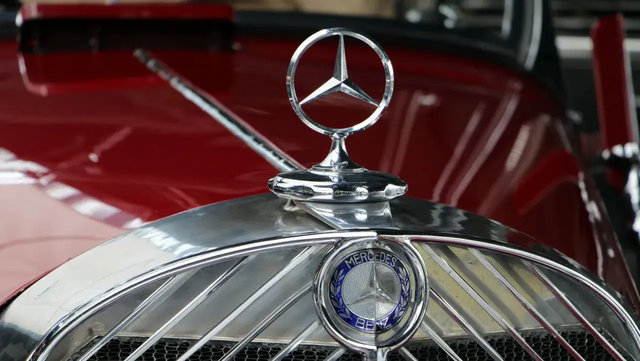Detaljerad bild av Mercedes-Benz-emblemet på en röd klassisk bil. Detta är ett av de första bilmärkena som skapades.