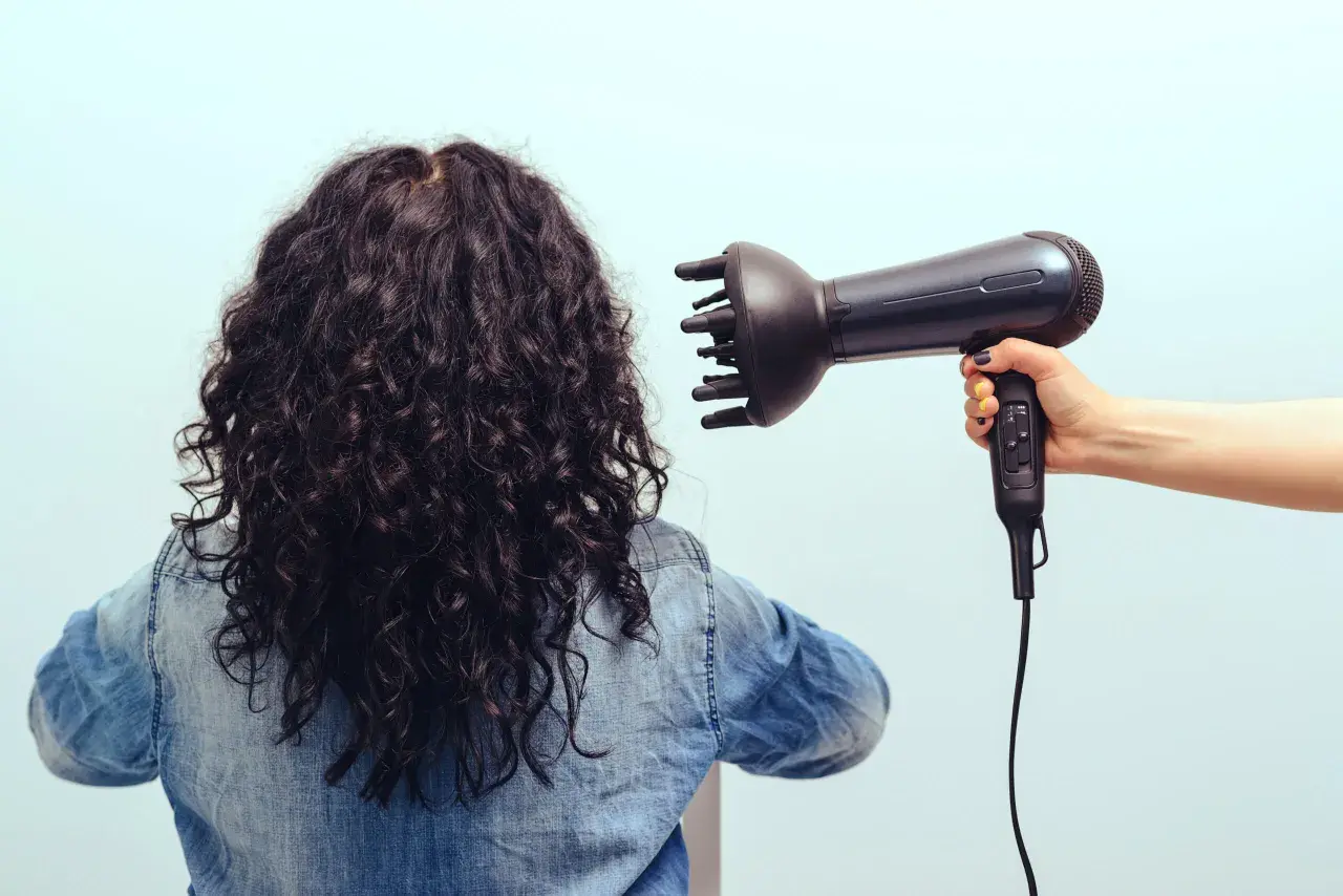 Donna con capelli ricci scuri viene asciugata con diffusore. Scopri come asciugare i capelli ricci per un risultato perfetto.