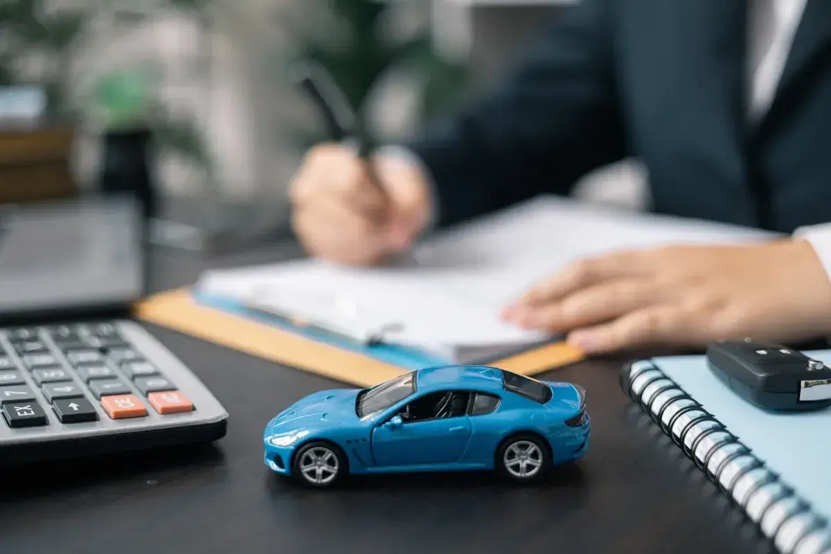 Niebieski model samochodu, kalkulator i kluczyki na biurku. Dłoń pisze na umowie, sugerując honda leasing.