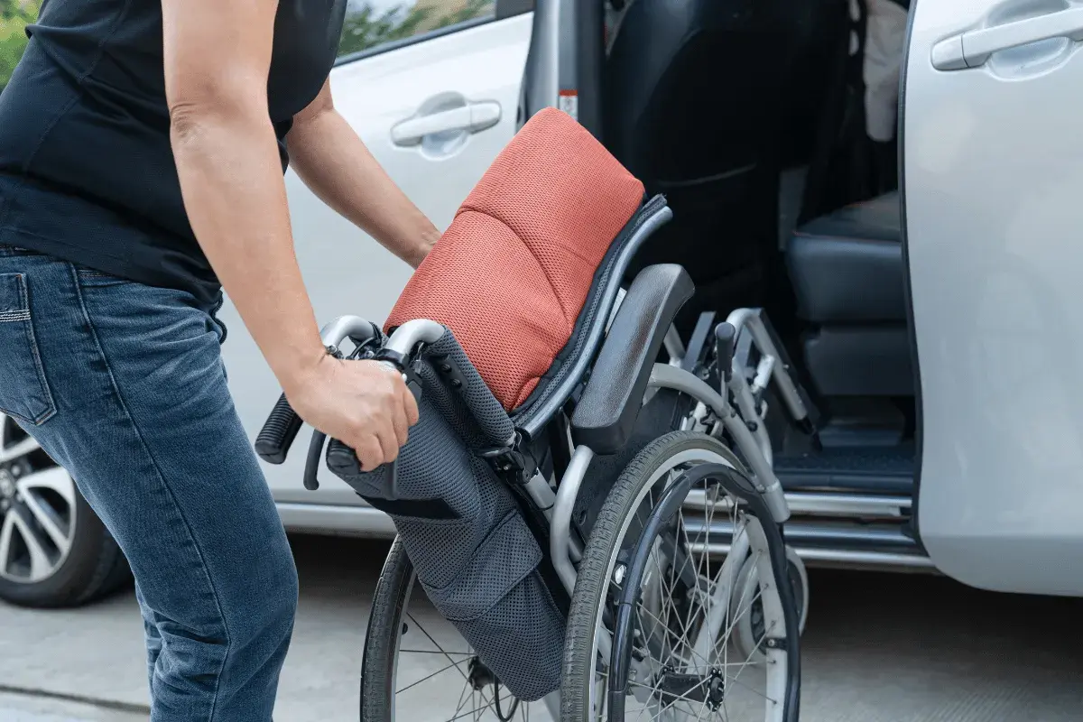 Persona piega una carrozzina vicino a un'auto, pensando all'assicurazione auto legge 104.