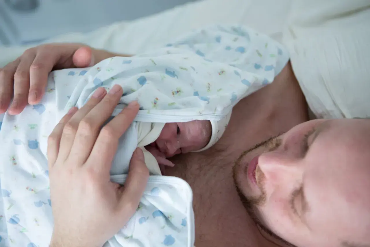 Ciepłe kangurowanie przez tatę po cesarce. Maluszek wtulony w klatkę piersiową ojca, czuje jego bicie serca.
