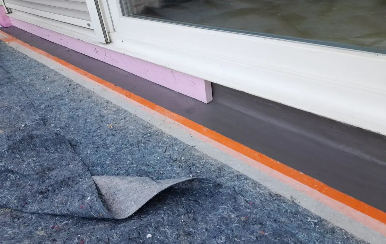 Schutzmatte liegt bereit, um den Sockel abzudichten. Dämmung und Abdichtung am Fenster sind sichtbar.
